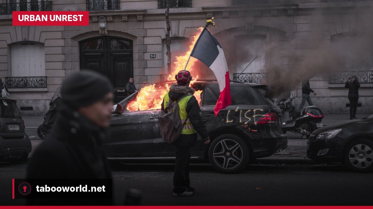 A street in a French city shows burning debris and masked figures amidst a backdrop of damaged buildings during widespread unrest.